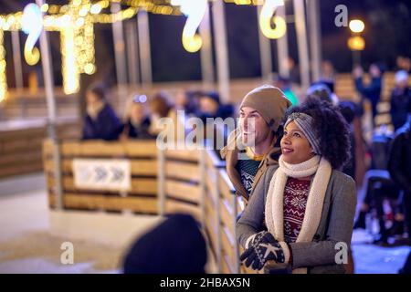 A young couple in love is enjoying beautiful atmosphere at ice-skating rink during christmas holidays on a beautiful night in the city. Christmas, New Stock Photo