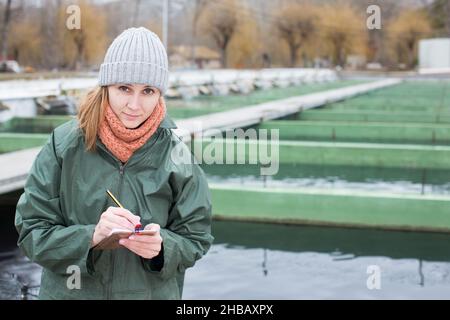 Female worker of fish farm writing something in notebook Stock Photo