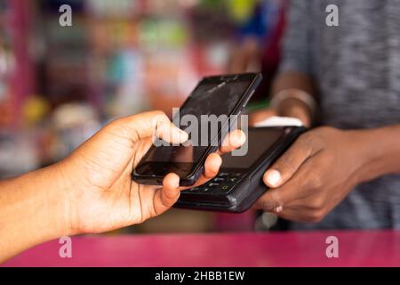Close up shot of hand paying money by taping mobile phone to swiping machine at retail Kirana or Groceries store - concept of contectless and one tap Stock Photo