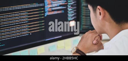 A male programmer sits and watches the code on a computer monitor to verify the program's execution. Stock Photo