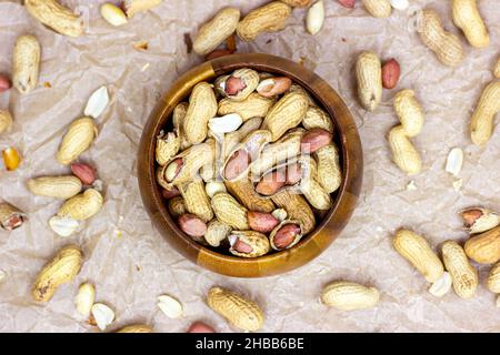Top view of unpeeled brown peanuts in the round wooden bowl on light background. Stock Photo