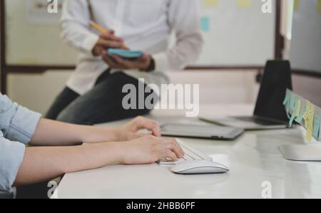 Hands working on computer keyboard and people sitting on the desk taking notes in the back, Office work concept. Stock Photo