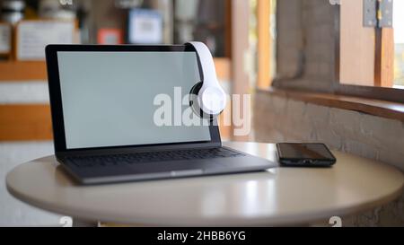 Mockup Laptop blank screen and headphone on screen, Laptop placed on a table in a cafe. Stock Photo