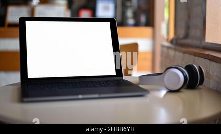 Mockup Laptop blank screen and headphone on placed on a table in a cafe. Stock Photo