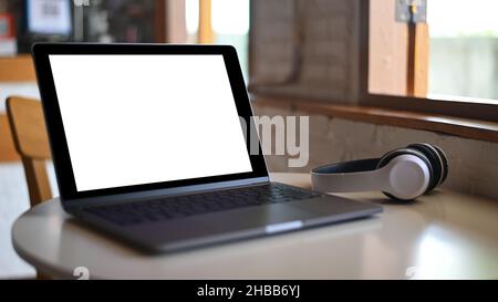 Mockup Laptop blank screen and headphone on placed on a table in a cafe. Stock Photo