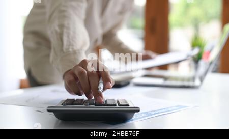 Close-up shot of Young man holding a pen and using a calculator placed in front,A man holding a pen and using a calculator. Stock Photo