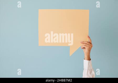 Unknown man raises his hand up holding speech bubble with copy space on light blue background. Stock Photo