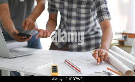 Two architects holding pencils and calculator are reviewing the house plan, The architects are helping design the house, The house plan and  laptop on Stock Photo