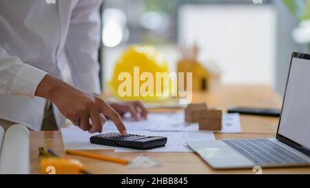 Young engineer is using a calculator to calculate house plans. Stock Photo