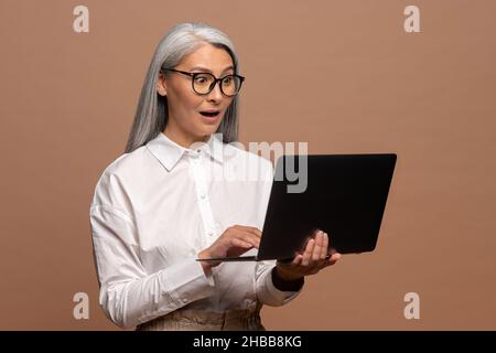 Portrait of the shocked surprised woman holding laptop and looking at display with big astonished eyes. Indoor studio shot isolated on beige background Stock Photo