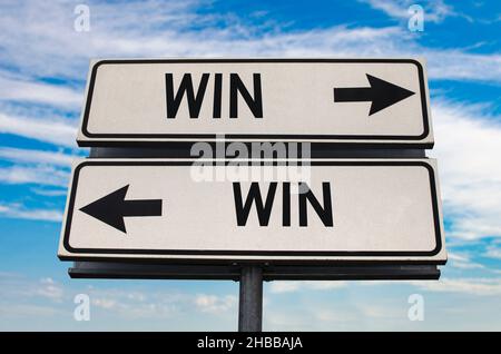 Win win road sign with two arrows on blue and grey sky background. White two street sign with arrows on metal pole. Two way road sign with text. Stock Photo