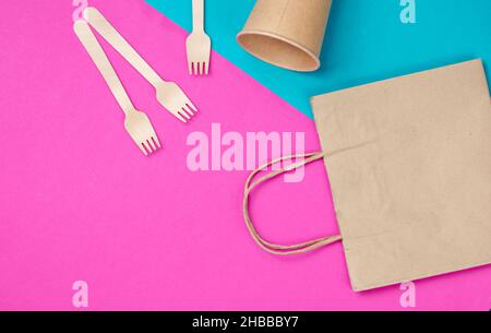 Disposable kitchenware of natural materials. Eco friendly concept. Wooden forks, empty craft coffee cup, bag on blue pink background. Top view Stock Photo