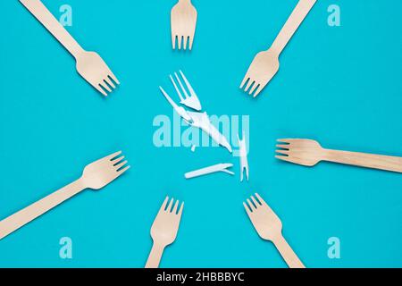 Minimalistic ecologically clean still life. Pop Art. Broken plastic fork among many wooden forks on blue background. Cutlery made from natural materia Stock Photo