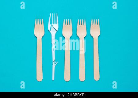 Minimalistic ecologically clean still life. Pop Art. Broken plastic fork among many wooden forks on blue background. Cutlery made from natural materia Stock Photo