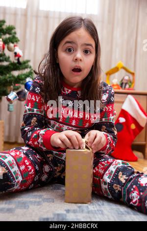 Caucasian little girl with amazed face opening Christmas day gift. Stock Photo