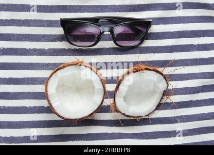 Two halves of chopped coconut and sunglasses on striped background Stock Photo