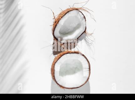 Minimalistic tropical still life. Halves coconut with shadows from palm leaves on white background. Creative fashion concept. Top view. Stock Photo