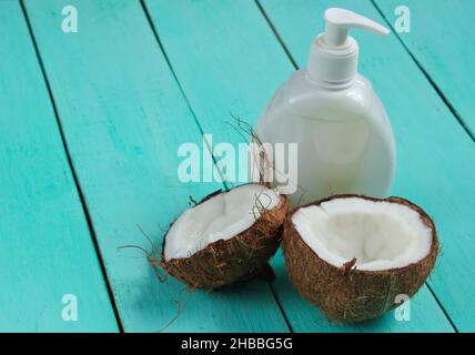 Two halves of chopped coconut and white bottle of cream on blue wooden background. Creative fashion concept Stock Photo