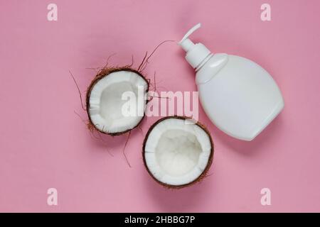 Two halves of chopped coconut and white bottle of cream on pink background. Creative fashion concept. Top view Stock Photo