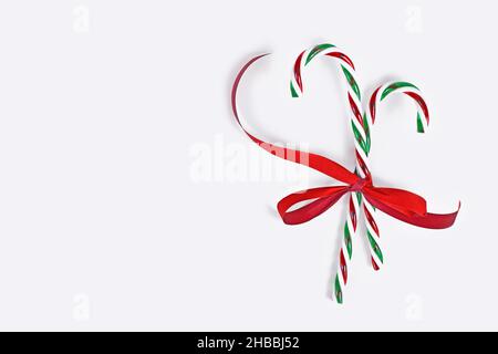 Striped candy canes tied together with red ribbon on side of white background with copy space Stock Photo
