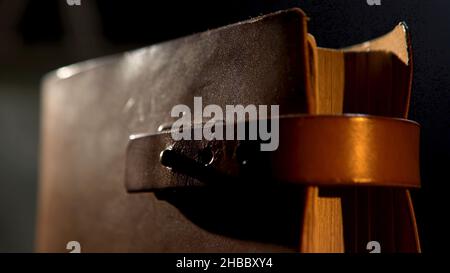 Vintage leather book with yellow pages. Close up of an ancient notebook with brown leather cover and a strap in vertical position isolated on black ba Stock Photo
