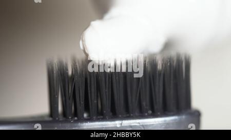 Extreme close up for a black toothbrush with white toothpaste being squeezed on it on beige background. The black bristles of the toothbrush with whit Stock Photo