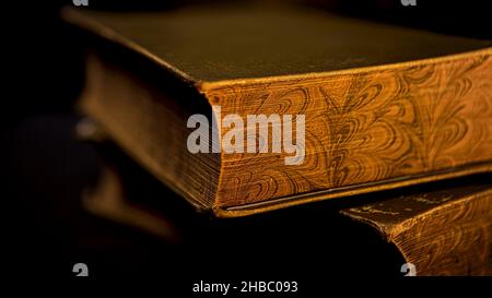 Close up of vintage thick book lying on flat surface isolated on black background. Side view of the edge of an ancient book with golden old pages. Stock Photo