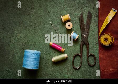 Old scissors, tailor tape and spools of thread on a dark green textured background close up, flat lay Stock Photo