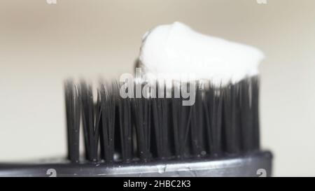 Extreme close up for a black toothbrush with white toothpaste being squeezed on it on beige background. The black bristles of the toothbrush with whit Stock Photo