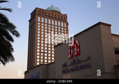 The Mall of Emirates, Dubai from the outside and a palm tree during a beautiful sunset. Color image of the building with it’s name and logo visible. Stock Photo