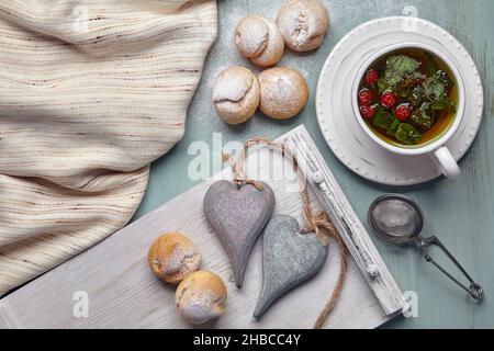 Delicious profiteroles with whipped cream and two decorative wooden hearts sprinkled with powdered sugar, with a cup of herbal tea and a tea towel on Stock Photo