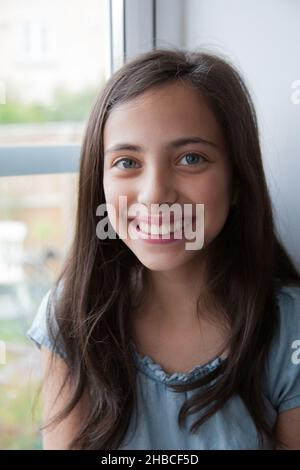 A portrait in a window of a mixed race girl with a big smile who is Caucasian, Asian and Black Stock Photo