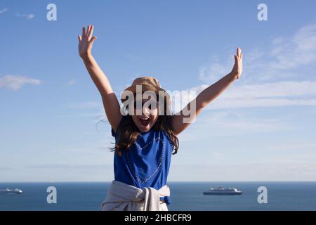 A girl with her arms in the air beside the seaside in Dorset in the UK, taken on the 3rd of August 2020 at Weymouth. Stock Photo