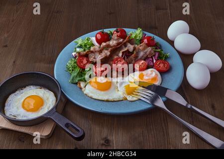 Fried eggs with bacon, lettuce and cherry tomatoes on a blue plate Stock Photo