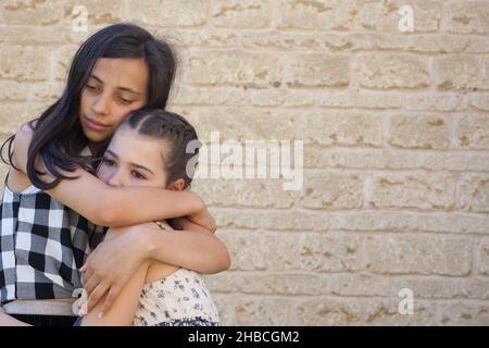 An older child hugs her sibling who is showing signs of sadness Stock Photo