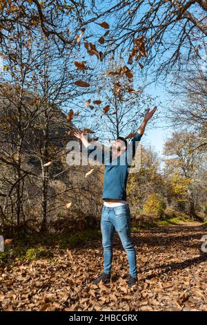 young man plays with yellow leaves falling down. vertical composition Stock Photo