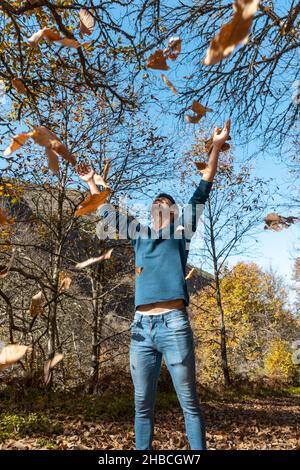 young man plays with yellow leaves falling down. vertical composition Stock Photo