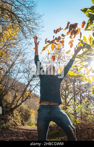 young man plays with yellow leaves falling down. vertical composition Stock Photo