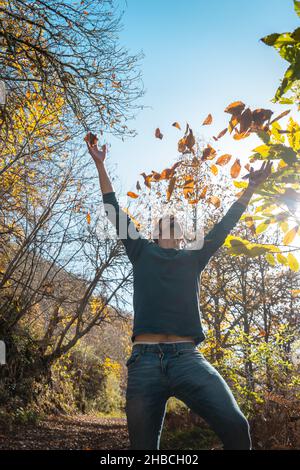 young man plays with yellow leaves falling down. vertical composition Stock Photo