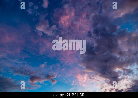 White and dark clouds colored pink and purple on blue sky during sunset Stock Photo