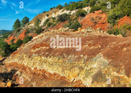 Triassic sedimentary layers of red, ochre and white rock, lined with Mediterranean scrub, in the Cerro de Vilarinha, Algarve, Portugal Stock Photo