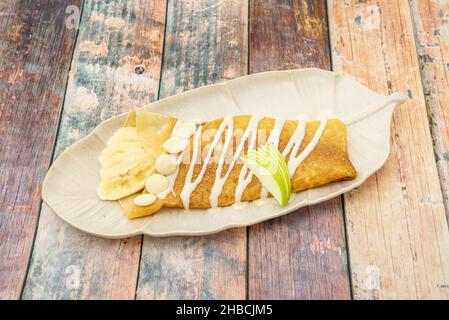 Recipe for crepes filled with chocolate syrup and sautéed banana slices, a very easy dessert to prepare perfect for a snack Stock Photo