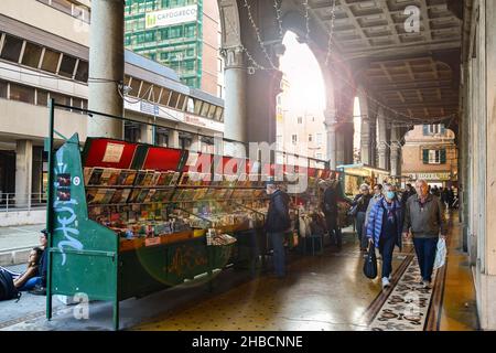 Backlit view of the arcade in Via San Vincenzo street with the stands of the book market and people in autumn, Genoa, Liguria, Italy