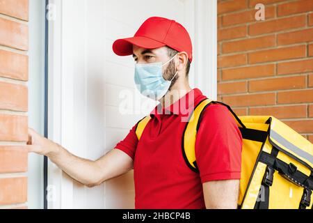 Young hispanic delivery food man in face mask ringing the doorbell Stock Photo