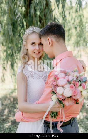 Bride and groom at wedding Day walking Outdoors on spring nature. Bridal couple, Happy Newlywed woman and man embracing in green park. Loving wedding Stock Photo