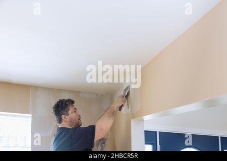 Man putting up a plasterboard a spatula on the white plaster on the wall. Stock Photo