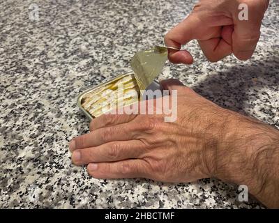 a can of sardines canned in olive oil is opened by a man's hands on a mottled marble table, horizontal Stock Photo