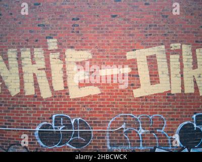 Yellow paint graffiti in Melbourne on a red brick wall with background patterns, Victoria, Australia. Stock Photo