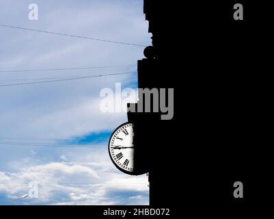 Round clock on the building with half of the dial in shadow from home against cloudy sky. Clock hand at 45 minutes. Concept- book cover, album cover. Stock Photo