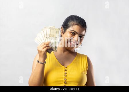 A beautiful Indian woman in yellow dress with cash smiling at the camera on white background Stock Photo